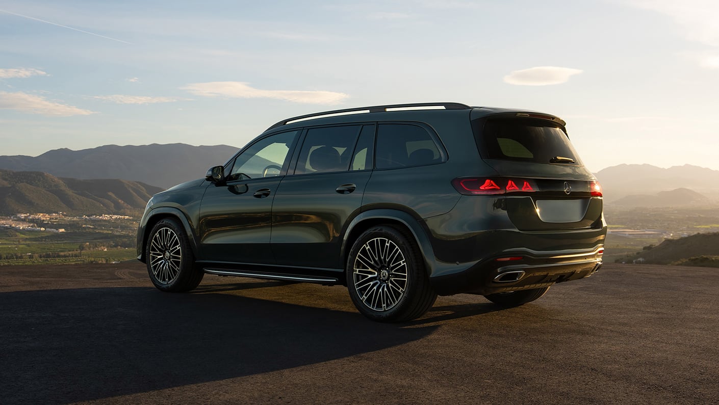 2027 Mercedes-Benz GLS in green, rear three-quarter view on a mountain overlook at sunset