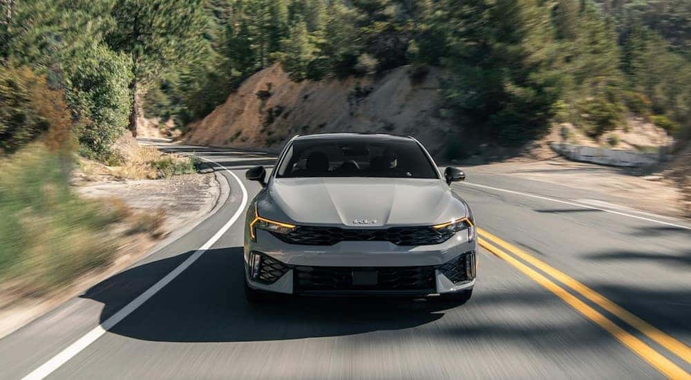 A gray 2024 Kia K5 is shown driving on a highway.