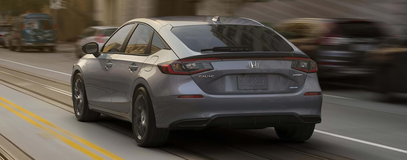 Gray 2025 Honda Civic Hatchback Sport Touring Hybrid driving in a city