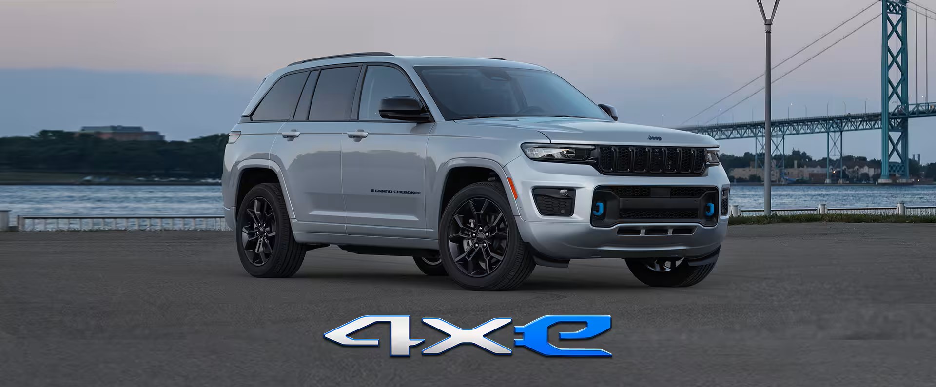 2024 Jeep Grand Cherokee 4xe parked by the water with a city bridge in the background, emphasizing its hybrid capabilities