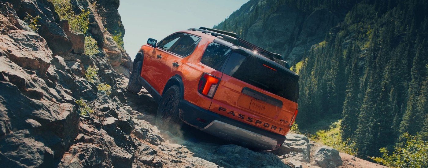 Orange 2026 Honda Passport TrailSport Elite driving on a mountain trail