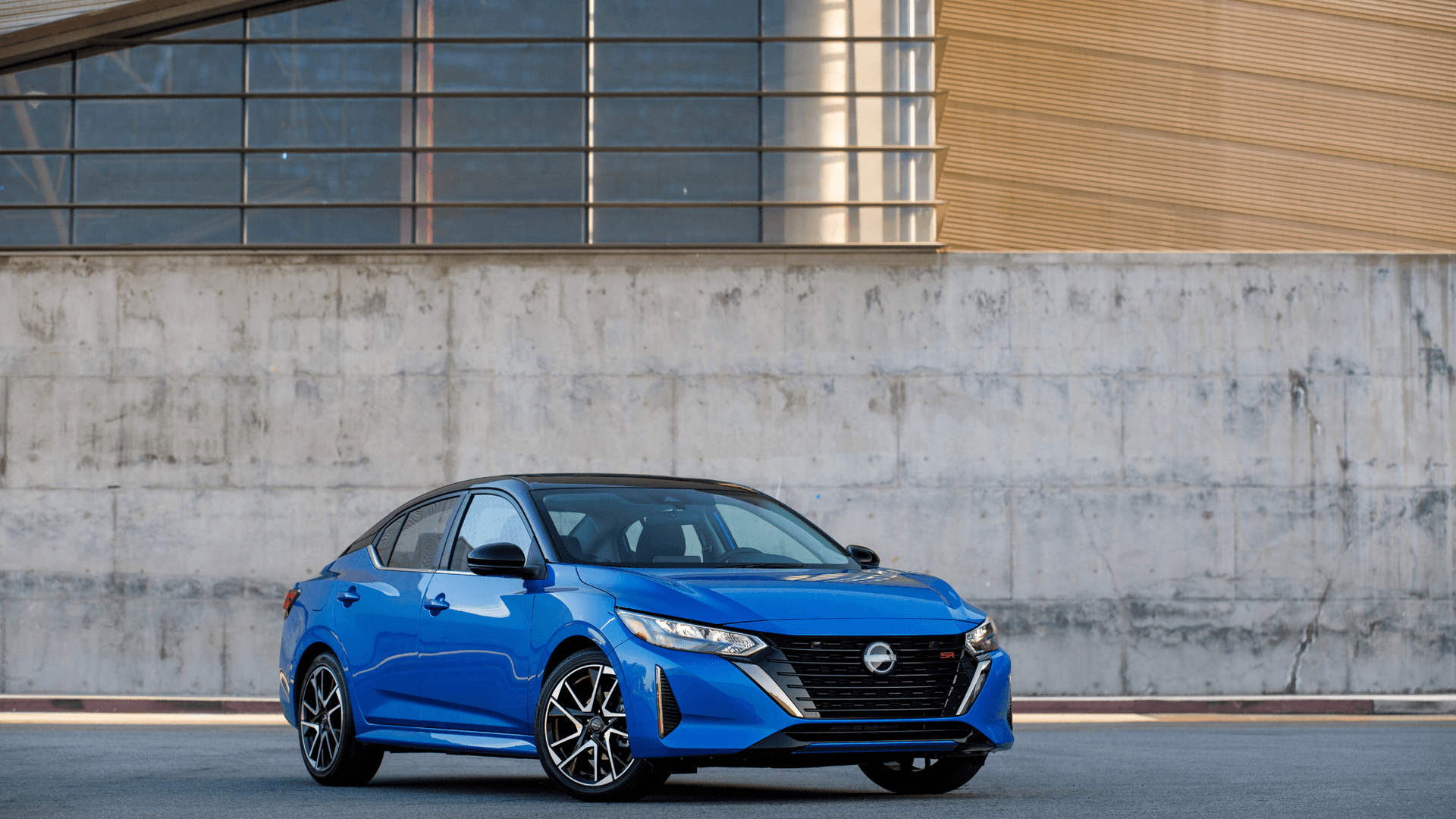 2026 Nissan Sentra® blue sedan parked in front three-quarter view beside a modern concrete building.