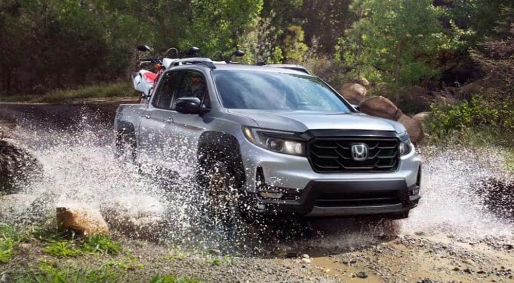 A grey 2024 Honda Ridgeline RTL-E driving over a shallow pond from a dealer with a Honda Ridgeline for sale.