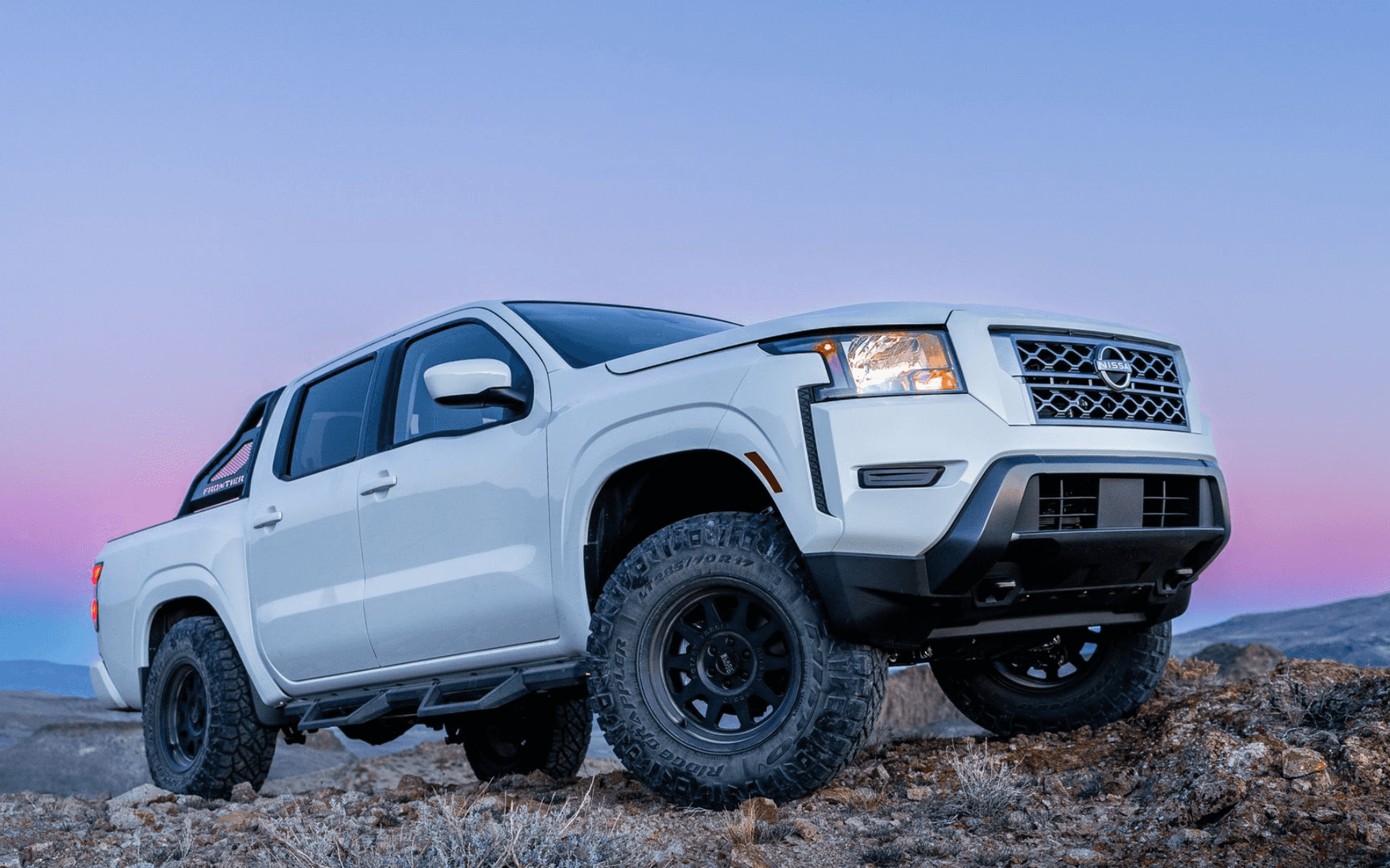 White Nissan Frontier off-road on rocky terrain at dusk