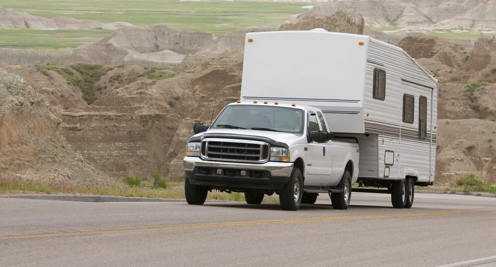 A white truck is carrying a white trailer, in the background you can see multiple rocky hills