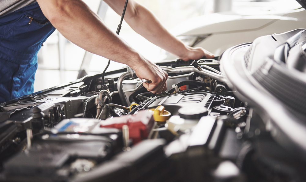 Man standing over engine, only torso and arms are visible, the hood is open and he is working on a part of the engine