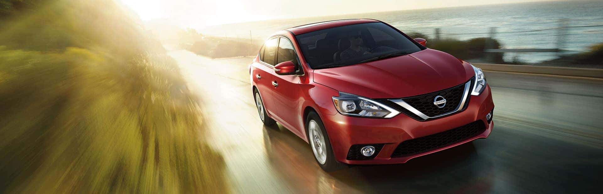 Red Nissan Sentra driving on an open road