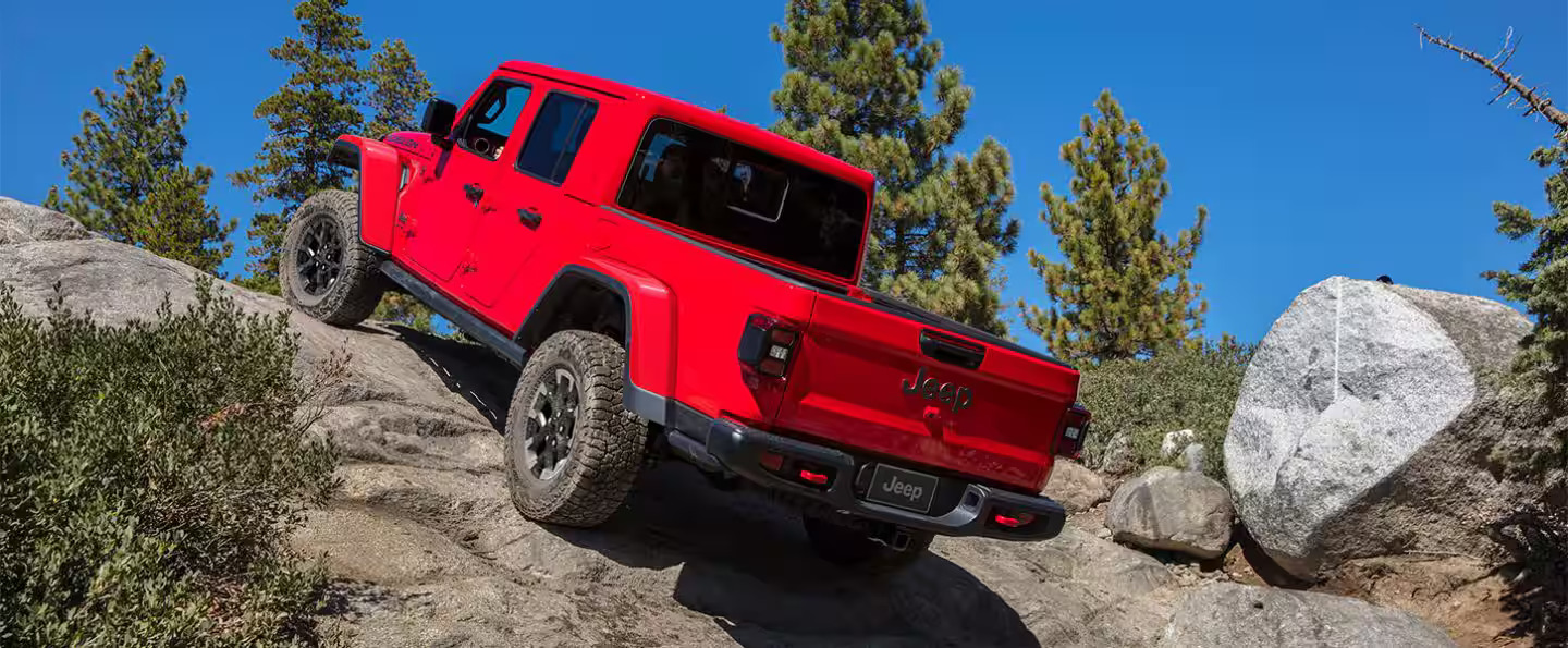 A red jeep driving up some rocks.