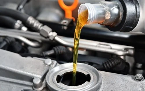 Fresh engine oil being poured from a plastic container into a car.