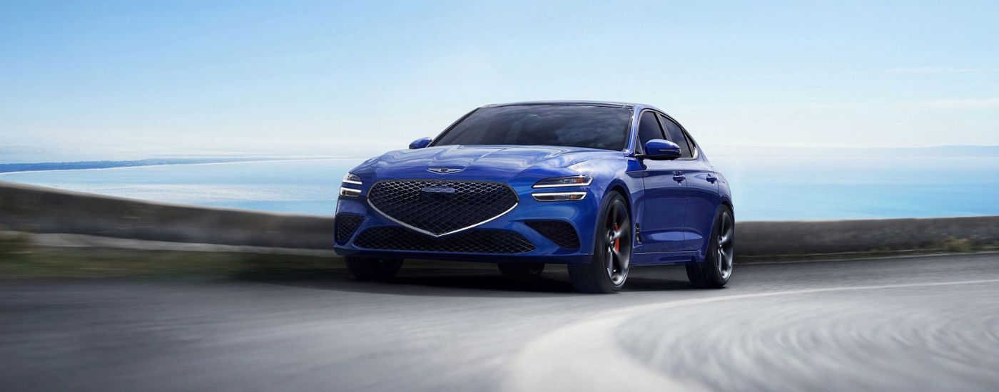 Blue 2024 Genesis G70 driving past an ocean