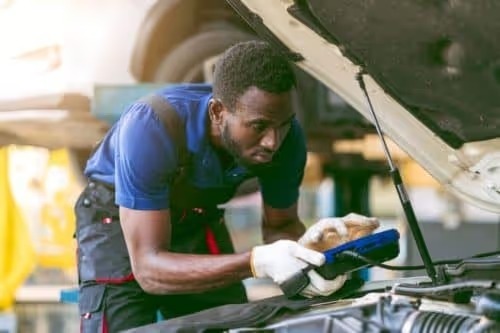 Technician checking a car battery with a diagnostic tool under the hood