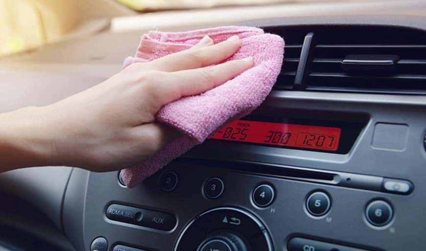 Hand wiping a car dashboard with a pink microfiber cloth