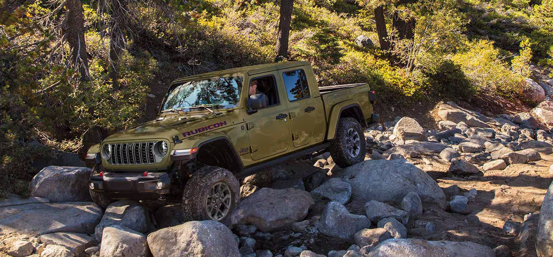 A green jeep driving on some rocks.