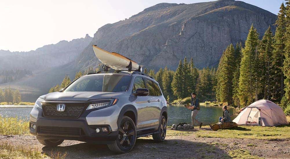 A silver 2021 Honda Passport is shown with a kayak on the roof at a camp site.