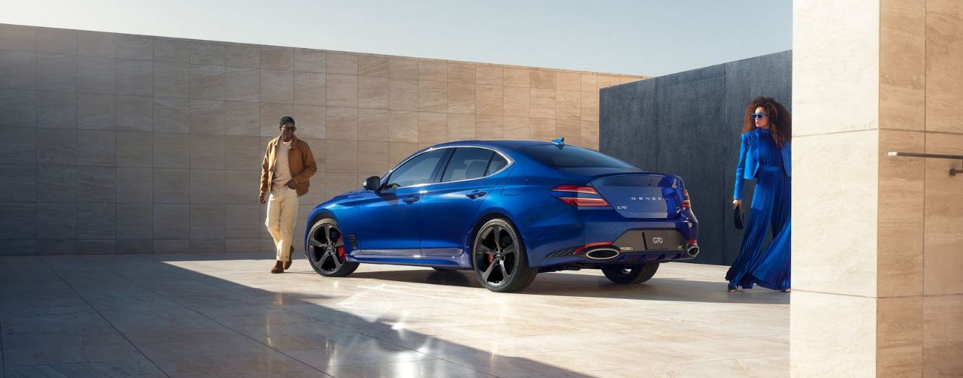 Two people walking away from a blue 2026 Genesis G70.