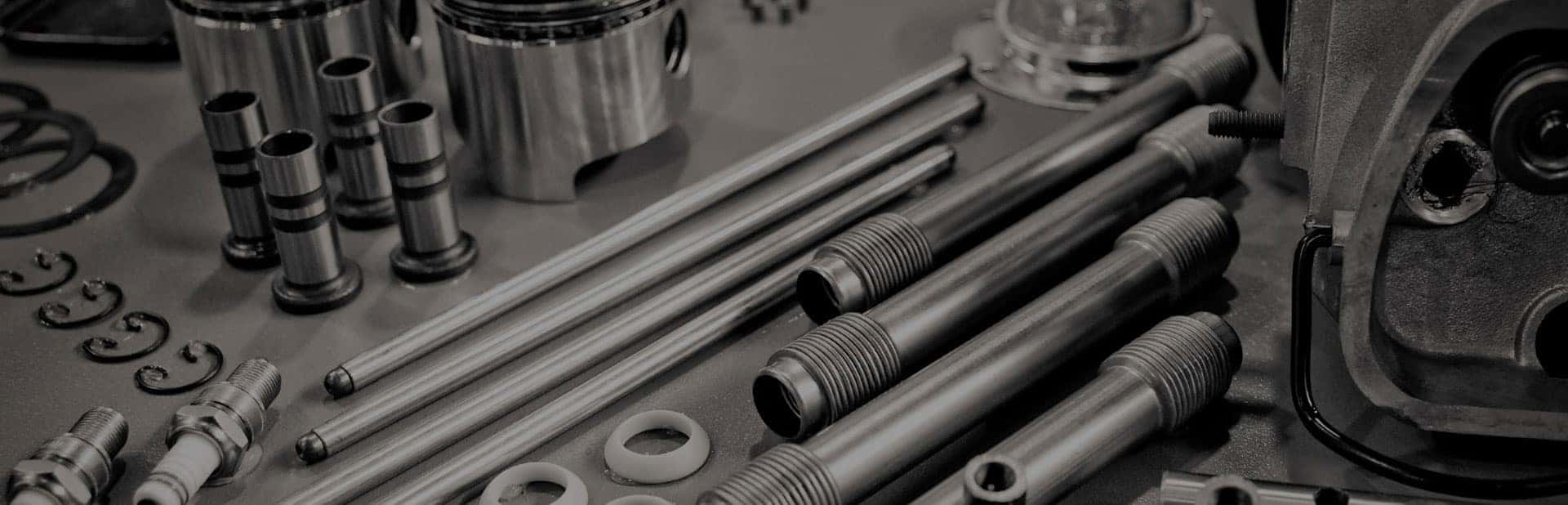 Nissan engine parts including spark plugs, valves and gaskets laid out on a dark workbench
