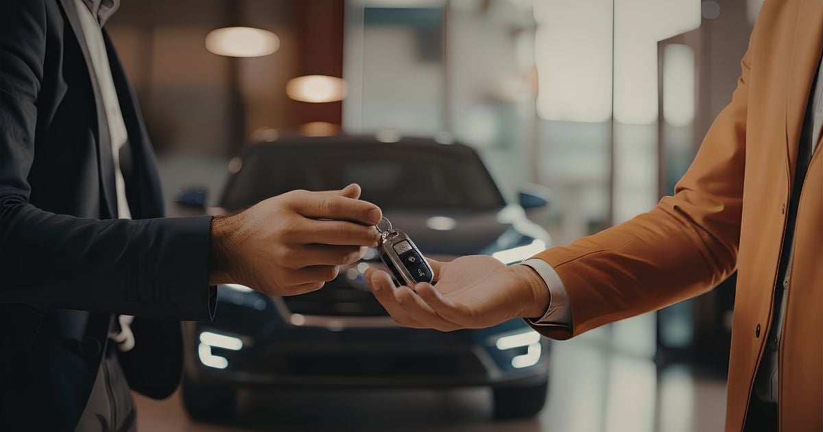 Salesperson handing car keys to a new owner in a dealership showroom