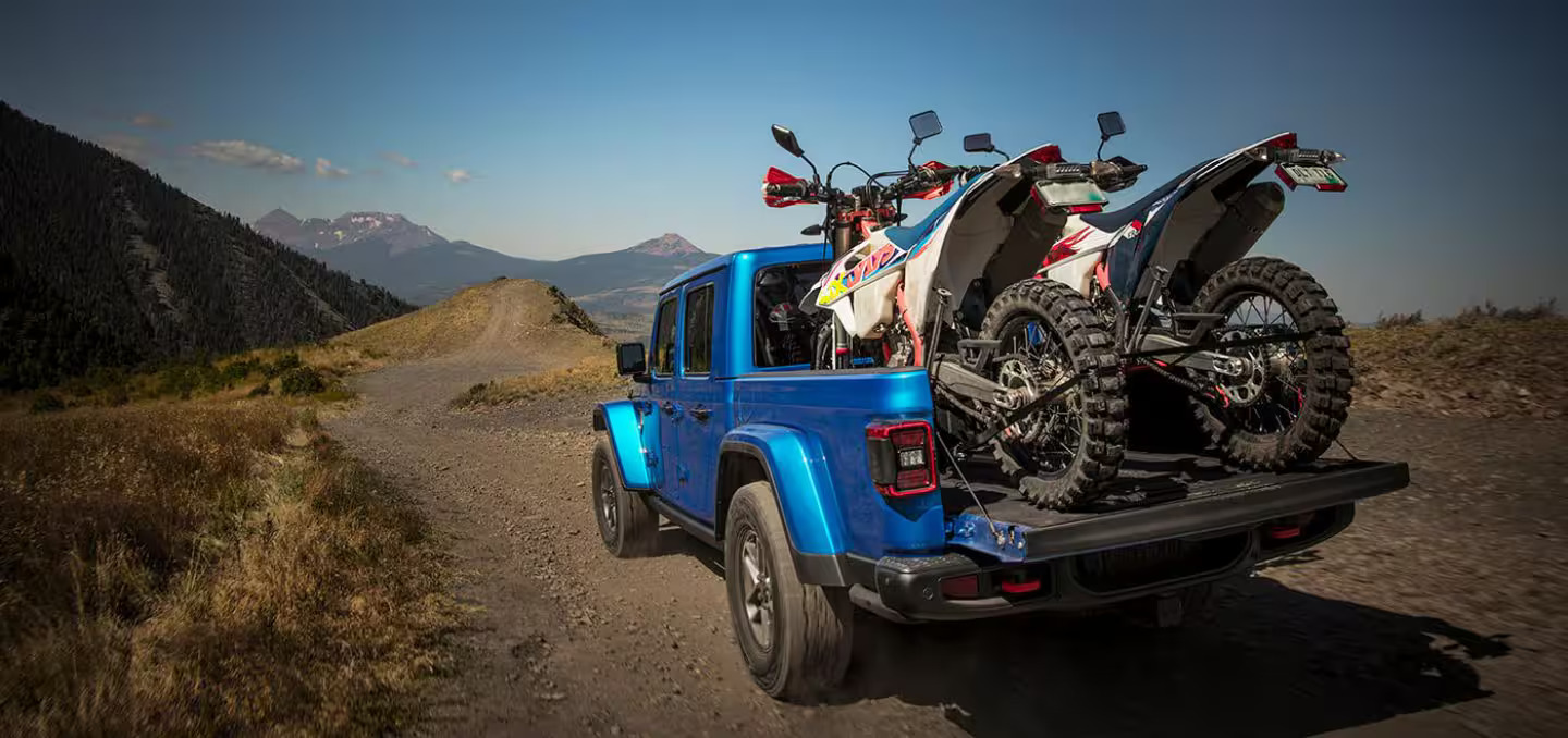 A blue jeep with two dirt bikes in the bed.