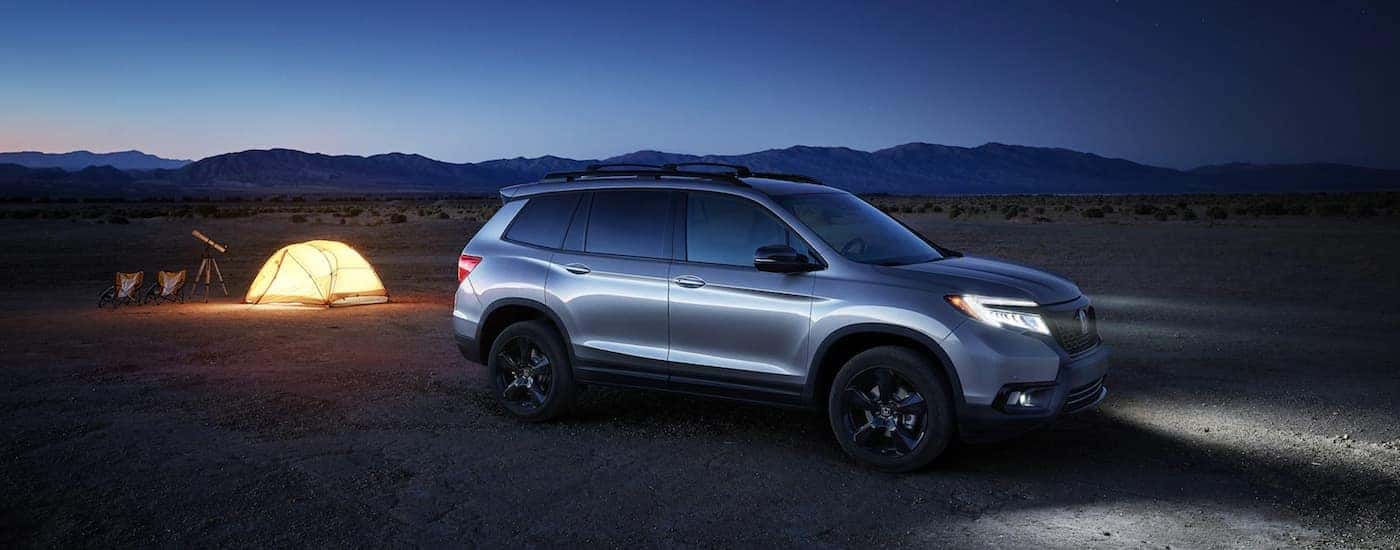 A silver 2019 Honda Passport is parked on the dirt next to an illuminated tent and telescope.