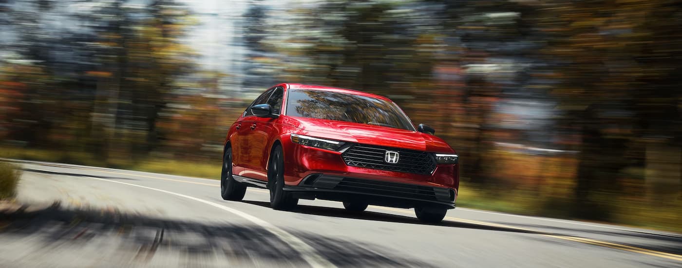 A red 2023 Honda Accord Sport L is shown driving on a winding road after leaving a Honda dealer near Clarence.