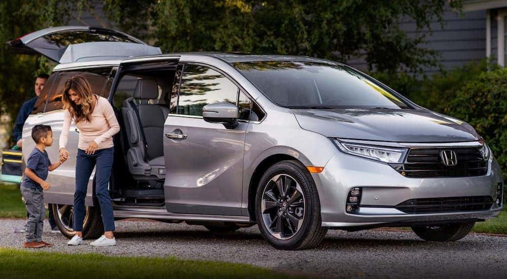 A silver 2022 Honda Odyssey Elite is shown from the side with the side door open next to a family.