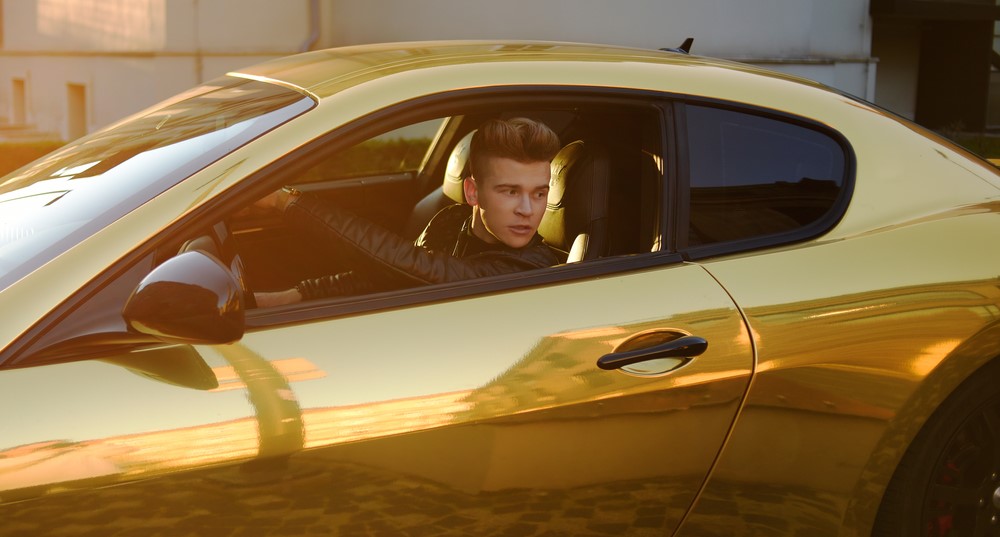 rich man driving gold car, looking over left shoulder