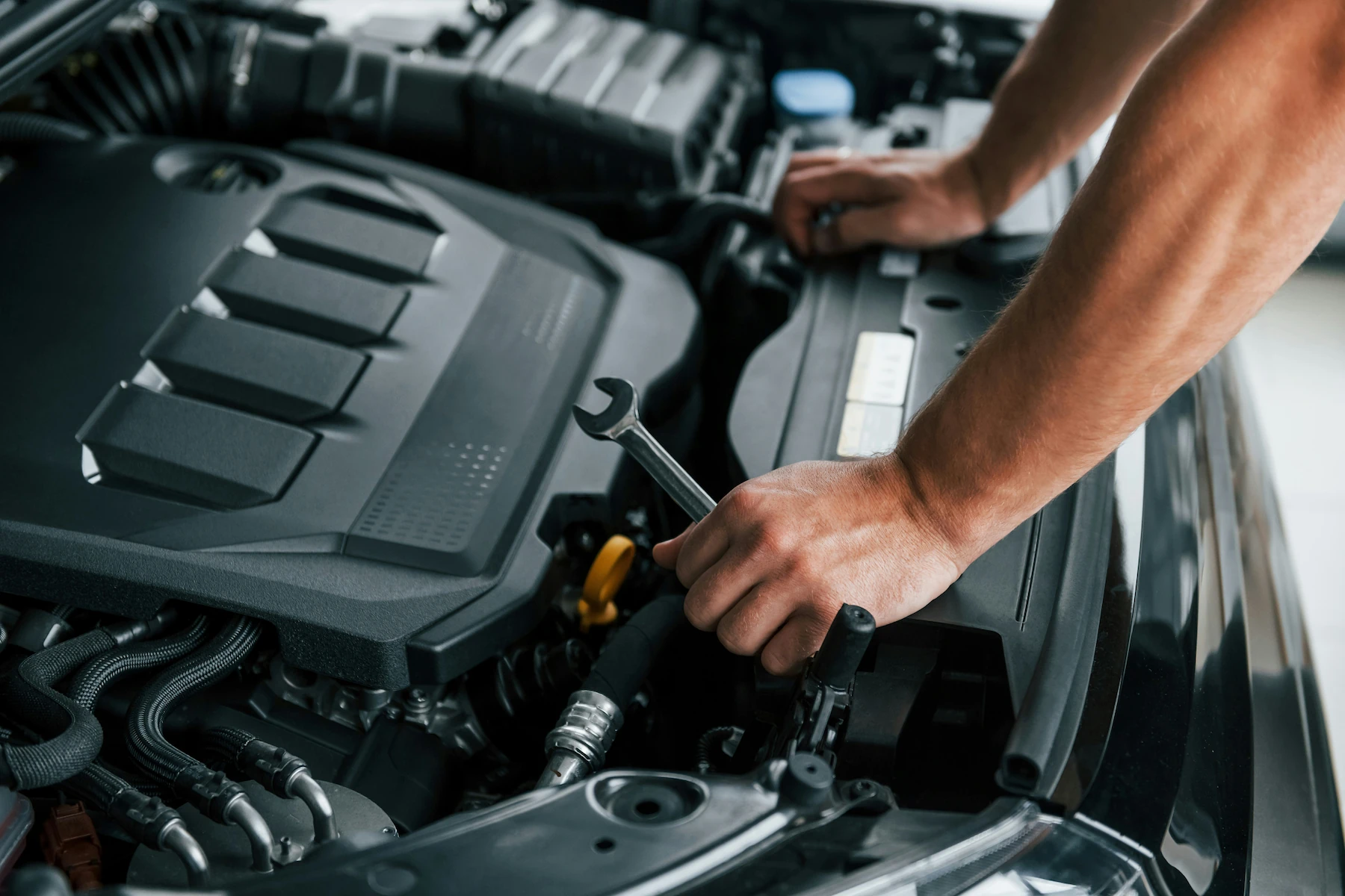 Close-up of a mechanic's hands using a wrench to tighten a hose clamp in a vehicle's engine bay, with a blue-capped fluid reservoir visible