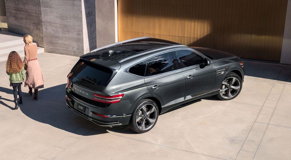 A gray 2027 Genesis GV80 parked by a garage.