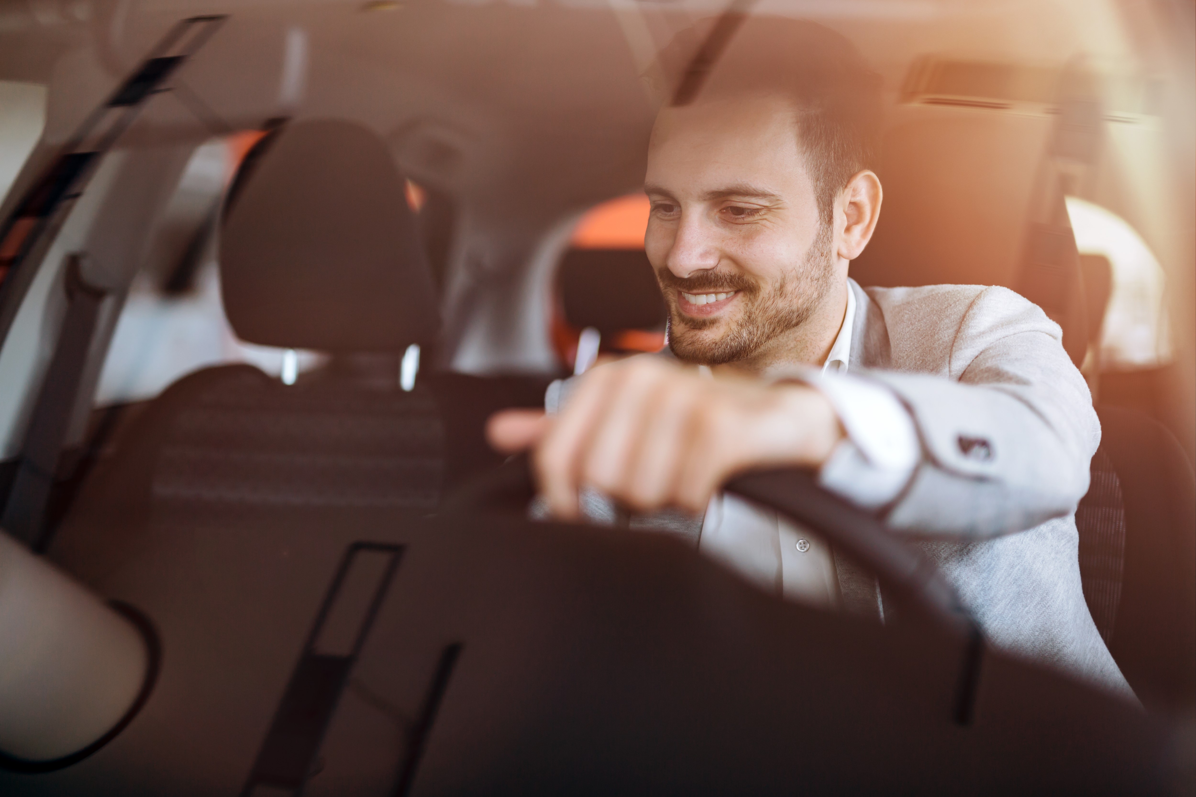 man with one hand on the steering wheel smiles as he changes the radio station in his vehicle