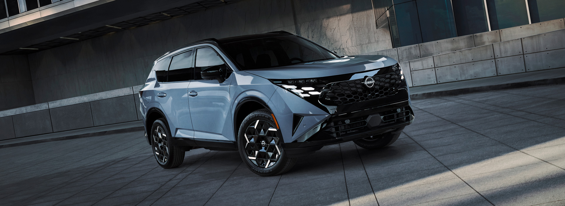 2027 Nissan Rogue in blue-gray parked outside a modern concrete building