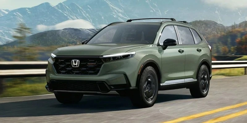 A sage green Honda CR-V driving on a mountain road at sunset