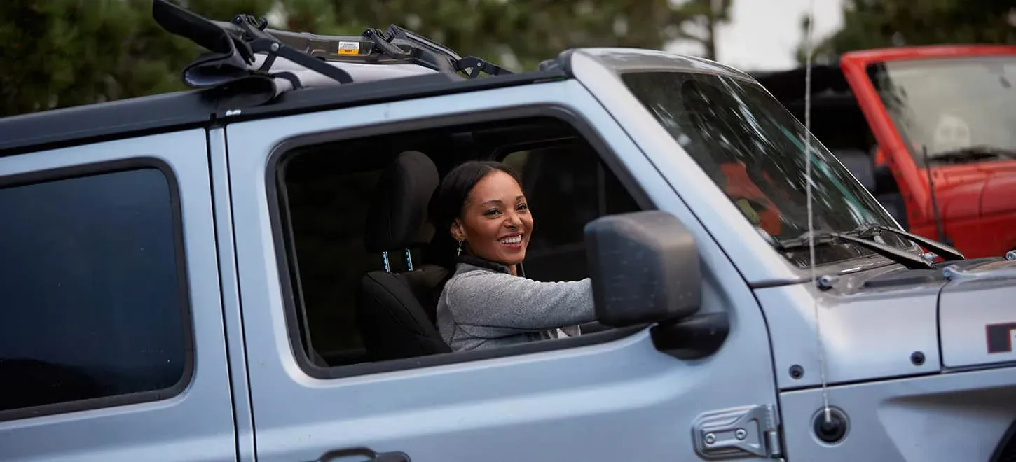 A woman driving a silver Jeep