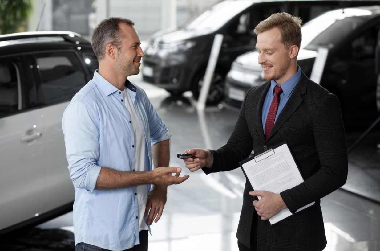 Salesman handing car keys to a happy customer in a dealership.