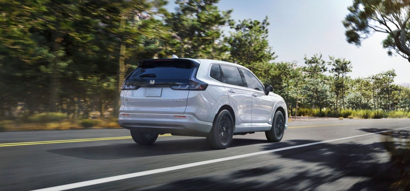 white 2025 Honda CR-V e:FCEV drives down a road in a wooded area