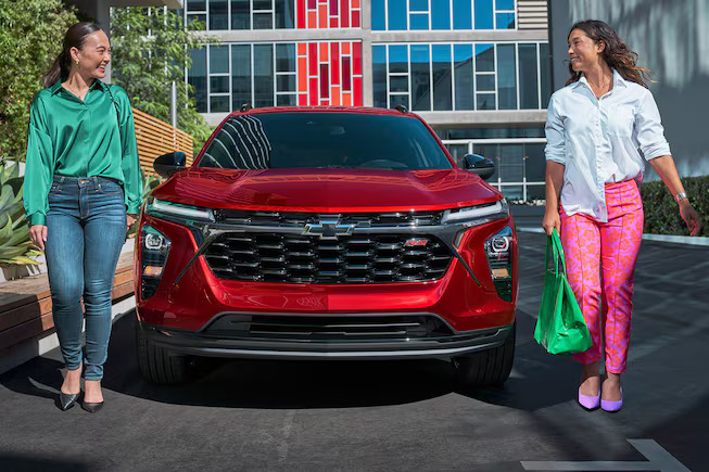 Two women walking by a red chevy trax.