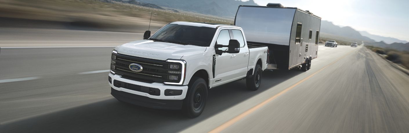 White 2025 Ford Super Duty Platinum Towing a Camper on a Highway