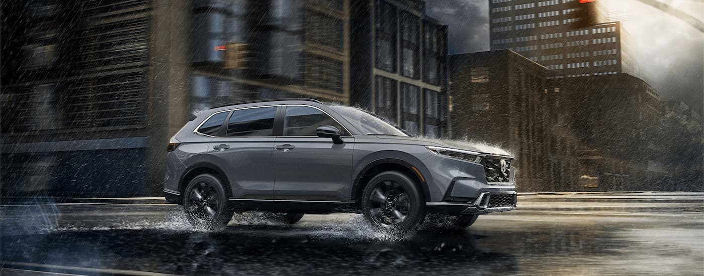 Grey 2024 Honda CR-V Hybrid driving on a city street in the rain