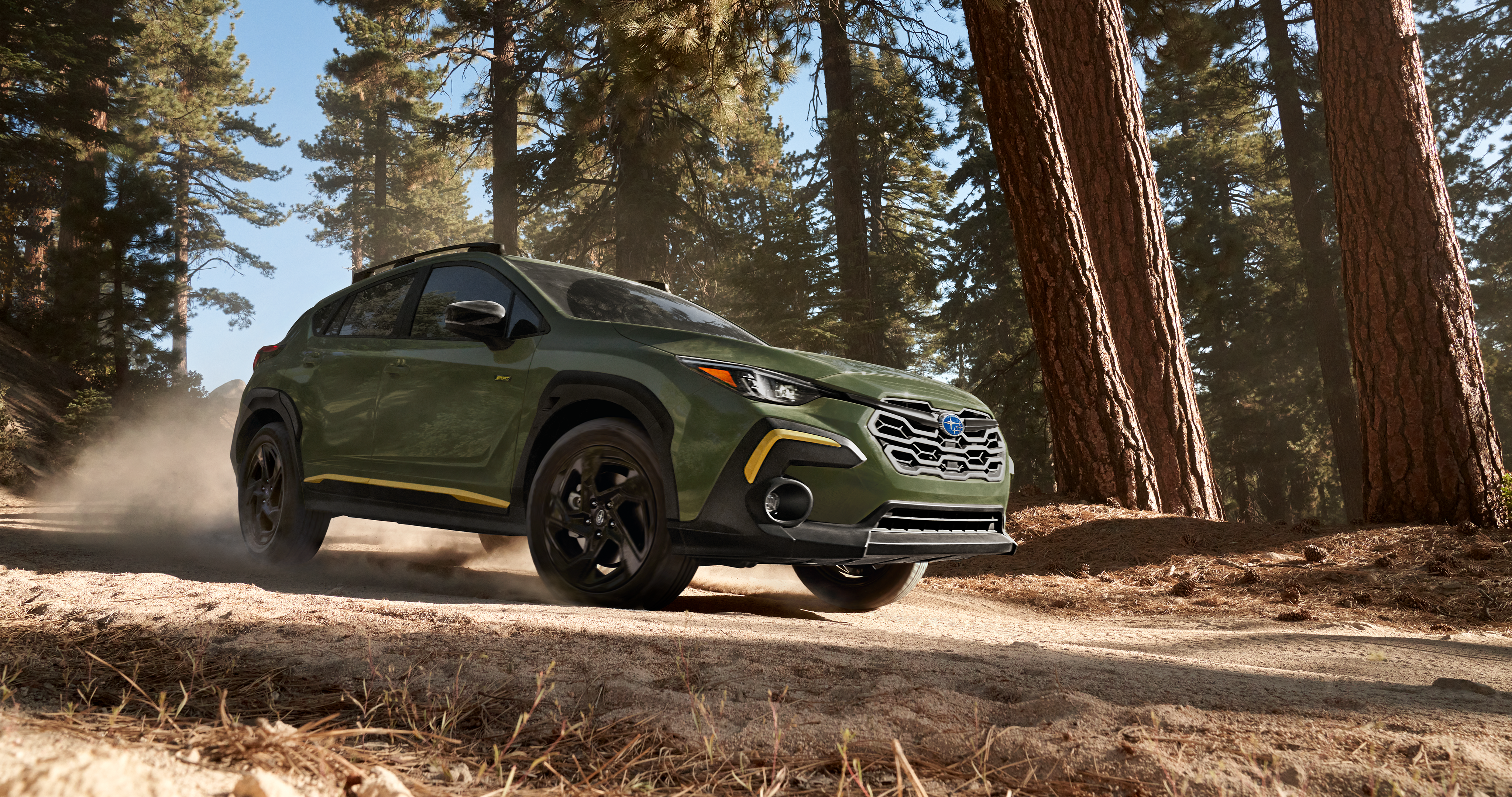25_CTK_hero_gallery_1.png / A 2025 Crosstrek Sport driving on a mountain road and through a forest.