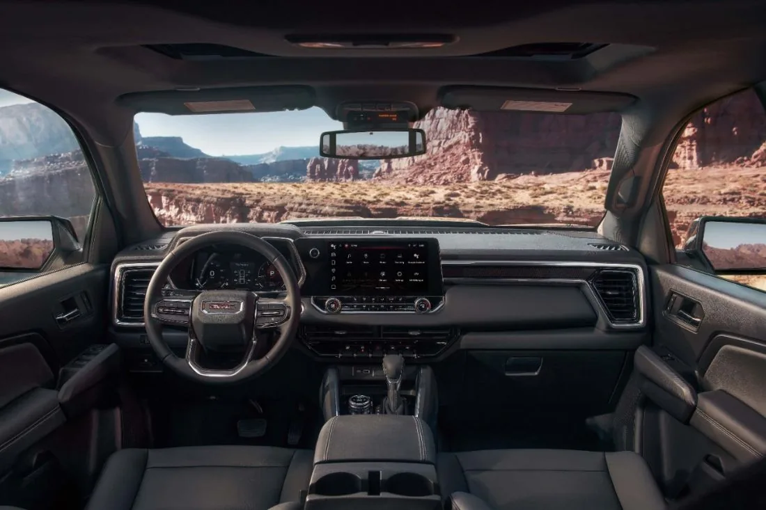 Interior view of a GMC pickup truck's cabin, showing the dashboard and touchscreen with a red rock desert canyon visible through the windshield