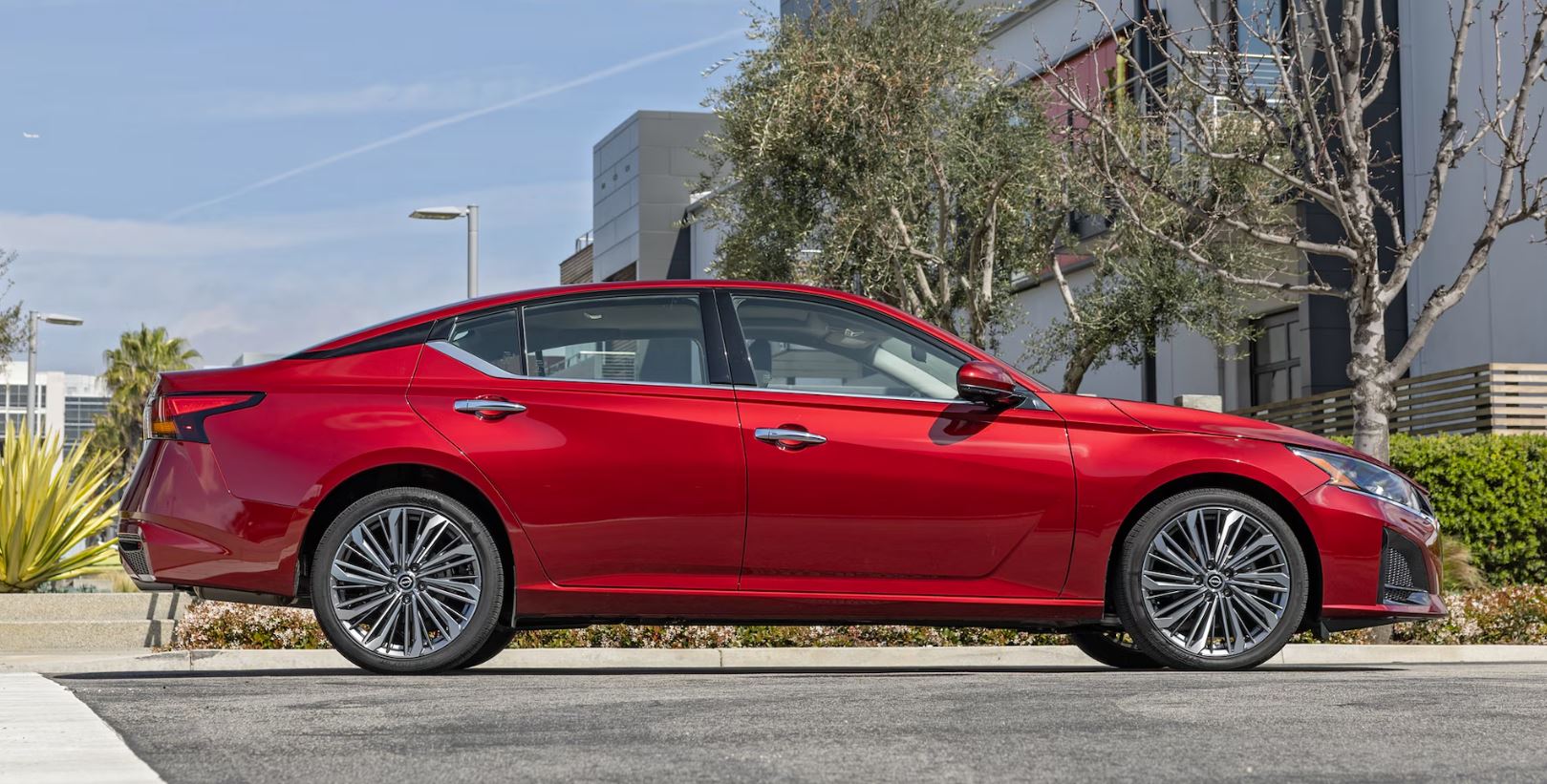 2024 Nissan Altima in a striking red color, parked in an urban setting with modern buildings in the background.