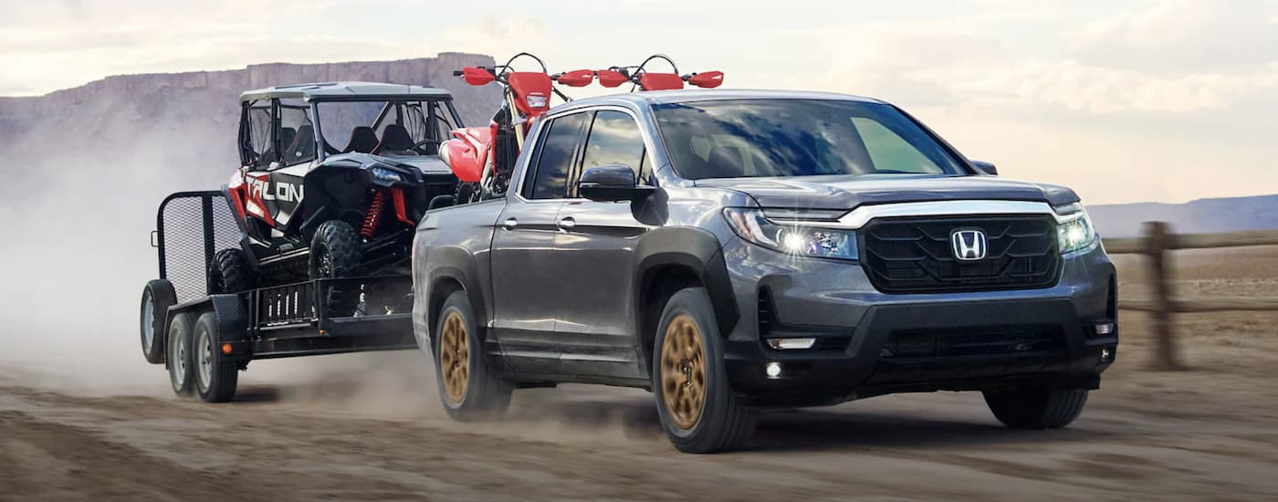 Grey 2022 Honda Ridgeline HPD towing a trailer on a dirt road 