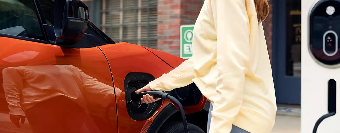 Woman plugging an EV charger into an orange 2026 Subaru Uncharted
