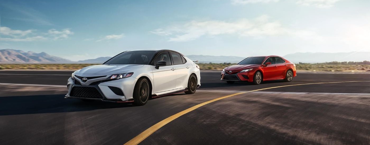  White 2020 Toyota Camry TRD and a red Camry are shown rounding a corner on a race track