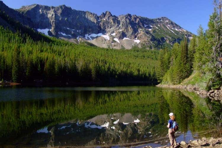 Hiker by a mountain lake reflecting rocky peaks