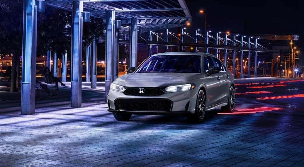 A silver 2025 Honda Civic for sale in Rochester is shown driving at night.