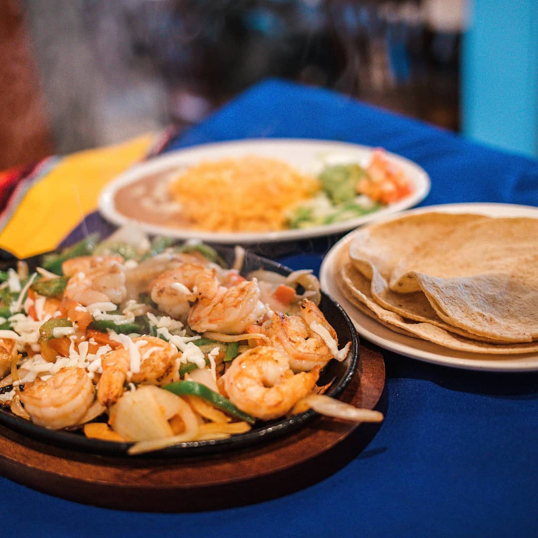 Shrimp fajitas with a side of rice, beans and guacamole; corn tortillas on the side