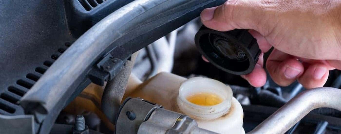 A mechanic is shown holding a reservoir cap.