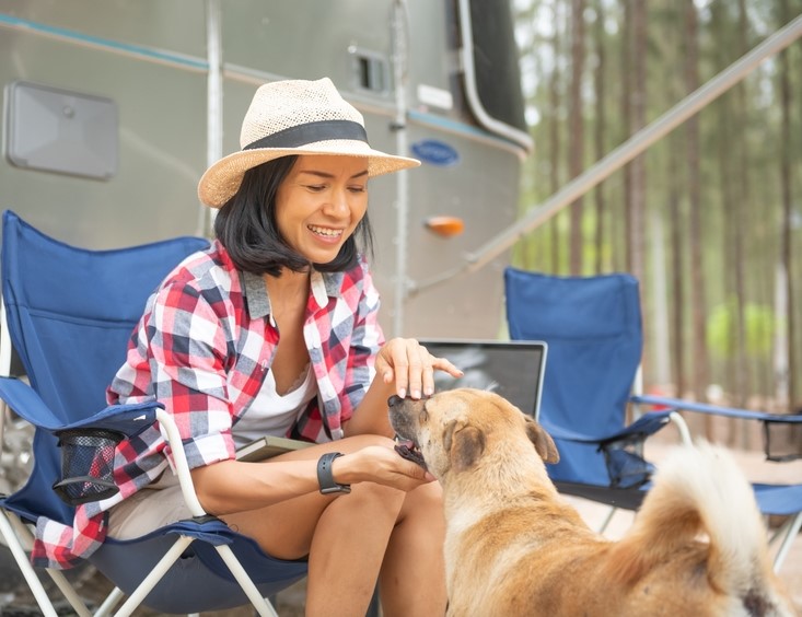 woman sitting in a lawn chari outside of her camper playing with her dog