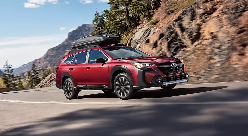 A red 2024 Subaru Outback Limited driving on a mountain road.