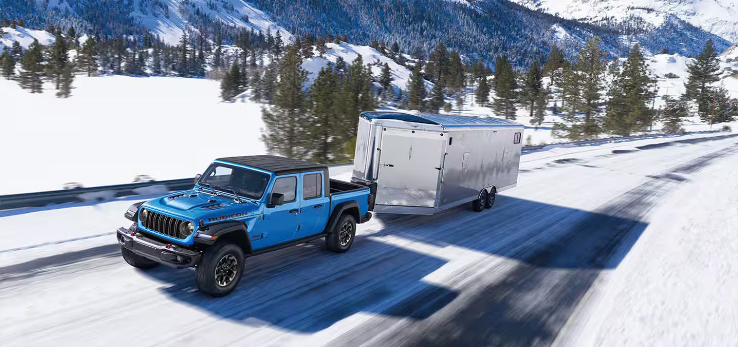 A blue jeep pulling a trailor in the snow.